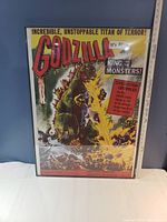 Full view of the framed Godzilla poster with title and illustrated scene of destruction, showing the object's overall condition and size.