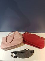 Photo showing a pink leather tote bag, a red handbag with gold chain strap, and a gray waist bag with black adjustable strap.