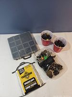 Hardware lot including braided rope, plastic organizer box with clamps and hardware, and two red cups with electrical connectors