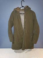 Front view of brown fur-lined winter jacket on hanger showing zipper partially open revealing fur lining inside hood and body.