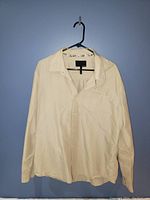 Front view of the Hurley men's long-sleeve button-up shirt hanging on black hanger against wall, showing light beige color and subtle vertical stripes.