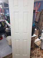 White six-panel interior door in a storage room setting with various items around it.