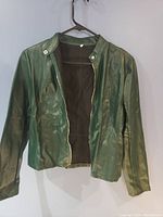 Front view of green faux leather jacket hanging on a hanger showing zip closure and snap button collar.