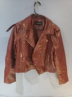 Front view of brown faux leather motorcycle jacket hanging on hanger against a blue wall.