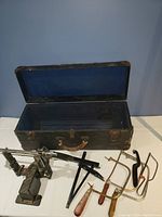 Black metal miter saw with base, two bow saws with wooden handles, and black carrying case.