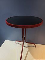 Full view of round patio table showing black glass top and red metal frame with three legs