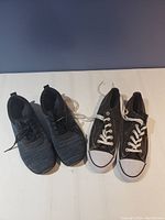 Top view of two pairs of men's shoes, one pair black knit athletic shoes and one pair black canvas shoes with white laces and toe caps.