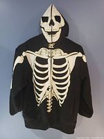 Front view of black zip up hoodie with white skeleton print showing chest skeleton and skull on hood.