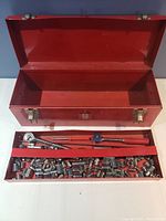 Open red metal toolbox with tray loaded with chrome sockets, wrenches, and adapters.