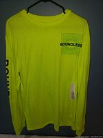 Front view of neon yellow long sleeve shirt on hanger showing 'BOUNDLESS' graphic on chest.