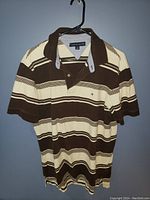 Front view of Tommy Hilfiger golf polo shirt with brown and cream stripes hanging on hanger