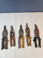 Five tin snips lined up horizontally showing handles and blade ends with wear.
