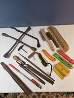 Various hand tools arranged on a white surface showing scrapers, wire brushes, files, corkscrew, knives, and other tools.