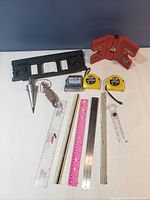 Close view showing Stanley tape measures, black Komelon tape measure, red magnetic angle locator with levels, and black plastic framing square.