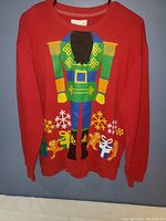 Front view of the red ugly Christmas sweater featuring a large nutcracker soldier graphic with snowflakes and presents surrounding it.