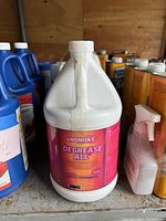 White 1-gallon plastic jug labeled UnsmoKE Degrease All positioned on shelf among other containers