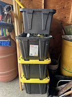 Stack of four black plastic storage totes, three 27 gallon HDX Tough Totes and one smaller tote with two yellow lids visible