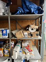 Photo showing white plastic sheeting rolls, drop cloths, and cardboard boxes holding plastic sheeting and trash bags on shelving.