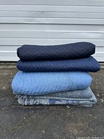 Side view of stacked folded moving blankets showing three quilted blankets and two felt blankets at bottom