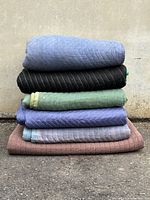 Stack of six quilted moving blankets folded and stacked showing different colors and textures.