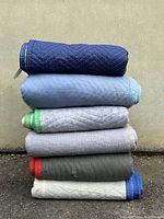 Stacked panorama of six quilted moving blankets in various colors from top view showing folded edges.