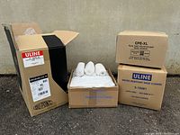 Wide view of open boxes with white rolled shoe covers and closed brown boxes labeled Uline with shoe covers and coveralls inside