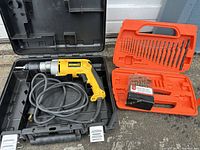 DeWalt DW235 corded drill inside black hard plastic case with two sets of drill bits in orange and black cases placed next to case.