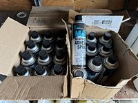 Two cardboard boxes containing black and blue cans of Abatix M4 Heavy Duty Adhesive Spray. Majority of cans appear full, one box new sealed.