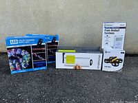 Photo showing all items included in lot, group shot: iReliev TENS system, SimpleHuman paper towel holder, LED rope light, and mini drone box.