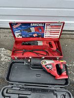 Milwaukee Sawzall in open red steel case with power cord, Skil reciprocating saw in black case below