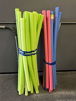Bundles of foam pool noodles in green, pink, and blue colors leaning against a wall.