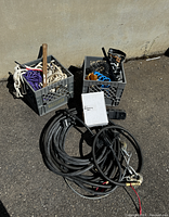 Overall view of the two grey crates containing ropes, hardware, airline tubing, and the large black extension cable coiled on ground.