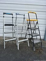 Three folding step stools standing side by side closed, showing color and structure details