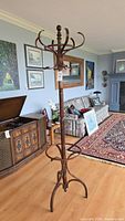 Full view of a tall wooden coat rack standing on a hardwood floor in a living room setting