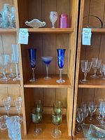 Shelved coloured glassware including blue tall glasses, green glasses, clear and pink hobnail glass, and etched pieces.