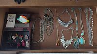 Top view of several chain necklaces and necklaces with pendants laid out on a table along with small boxes holding earrings and pins.