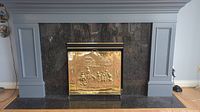 Brass fireplace screen installed in front of a fireplace with a dark stone surround and white mantle.