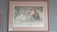 Framed winter scene wall art showing two women on a sleigh in a snowy village setting
