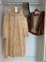 Photo of beige full-length fur coat, brown fur shawl/stole, and mink muff accessory hanging in closet