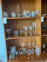 Full view of three shelves with assorted clear glassware including various stemmed glasses, short glasses, decanter and pitcher.