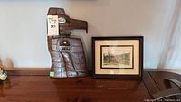 Photo of carved wooden eagle head sculpture and framed landscape print displayed on a shelf