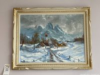 Framed oil painting showing the entire artwork and frame, depicting a snowy village with church and mountains.