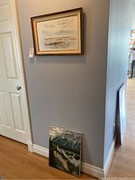 Wide photo showing two original art paintings, one hung on wall and one leaning against wall