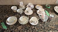 Overview of various tea cups on saucers, cream pitcher, and sugar bowl arranged on granite countertop