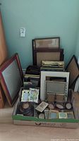 Wide view of multiple photo frames stacked upright and lying in a box including large frames leaning against wall.