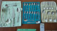 Wide view of all silver plated spoons and utensils arranged in three cloth trays showing full variety in the set.