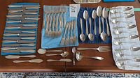 Overview of entire silverware set laid out on table with knives, forks, spoons, and serving pieces visible