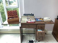 Wide shot of the Singer sewing table with the sewing machine, sewing supplies basket, sewing patterns, and foot pedal on the floor below the table.