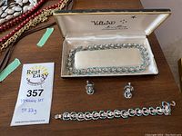 Overall view of sterling silver jewelry set including necklace in presentation box, bracelet, and clip-on earrings.