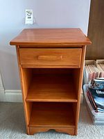 Front view of a wooden side table showing drawer and two open shelves.